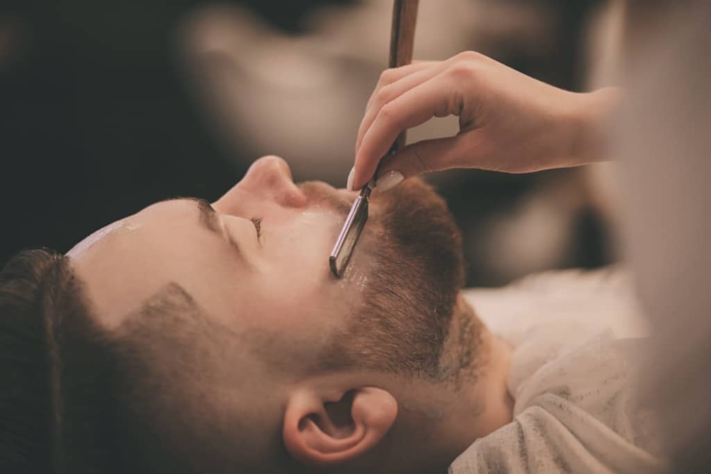 hipster man with a beard on a chair in the barbershop while shaving beard