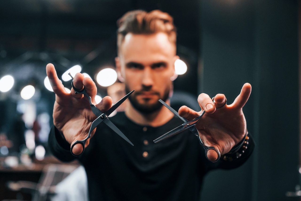 young-bearded-man-standing-in-barber-shop-and-holding-scissors.jpg